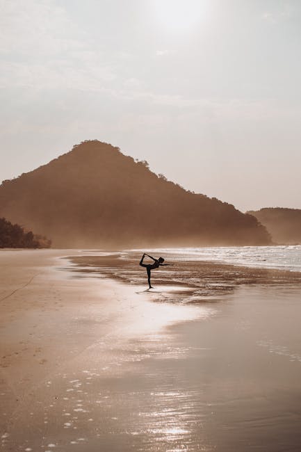 Woman in a yoga pose on a wooden deck by the water at sunrise.